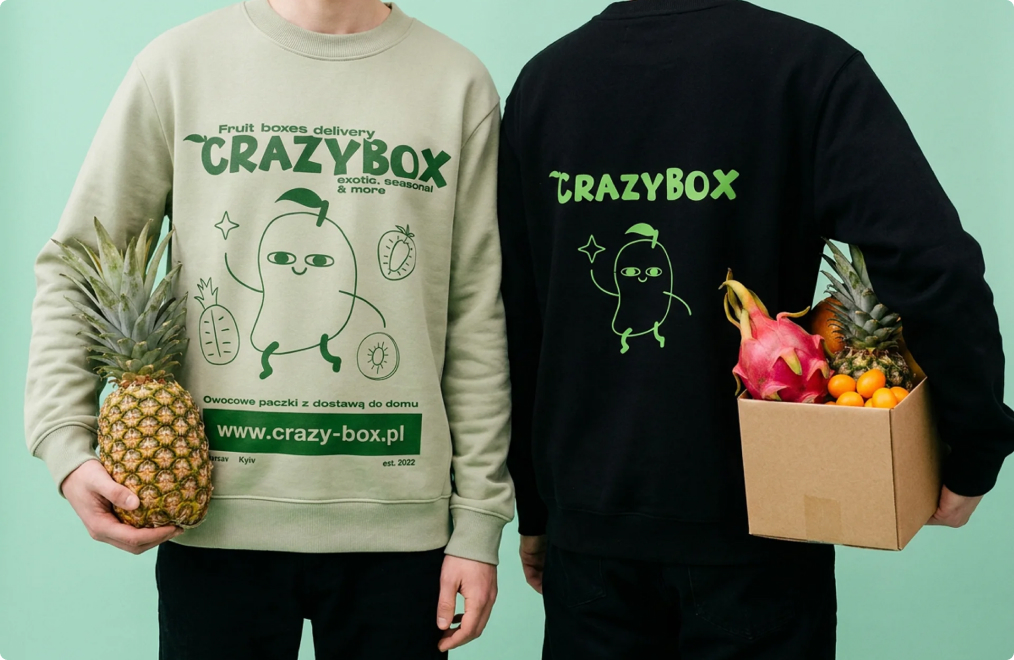 Two people in CrazyBox sweatshirts, one holding a pineapple, the other a box of fruit